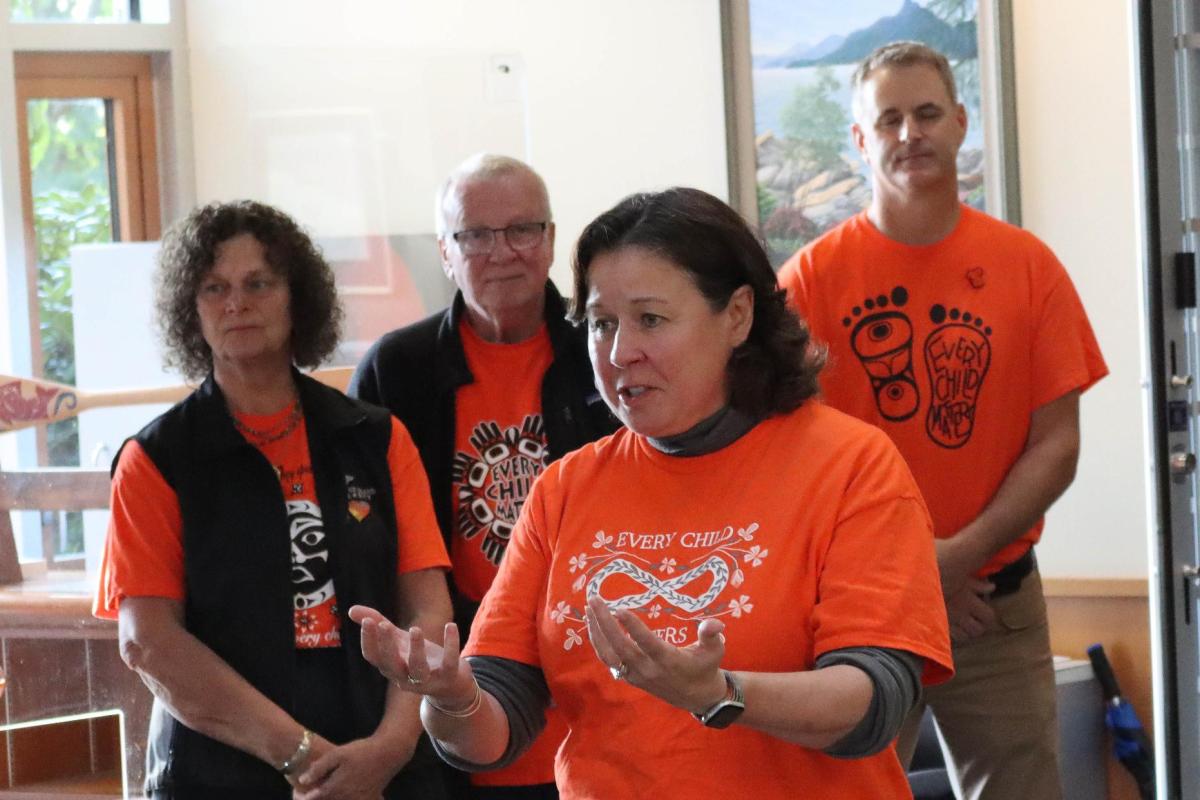 President Saucier speaks with her arms raised, wearing an orange shirt