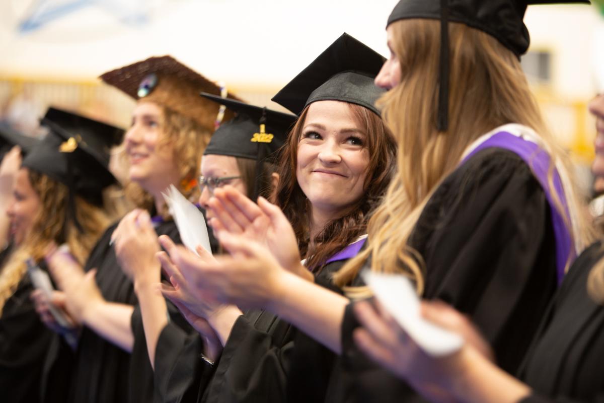 Graduates wearing caps and gowns clap and smile