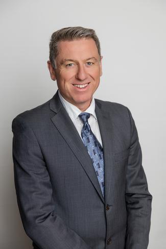 Portrait of Mark Walsh in a grey suit, blue tie, smiling.