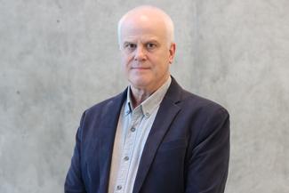Chris Jaeger smiling, wearing a navy blue suit in an airy modern room