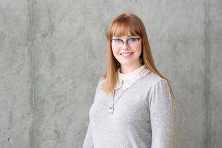Heather Wiebe smiling wearing glasses and a grey sweater in an airy, modern room