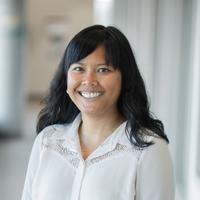 Sarah Mei Lyana, smiling, wearing a white shirt and blue jeans against a neutral background