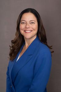 Lisa Marie Barron smiling, wearing a blue suit with a dark grey background