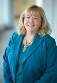 Sharon Torgerson, smiling, wearing a teal suit in an airy, modern room